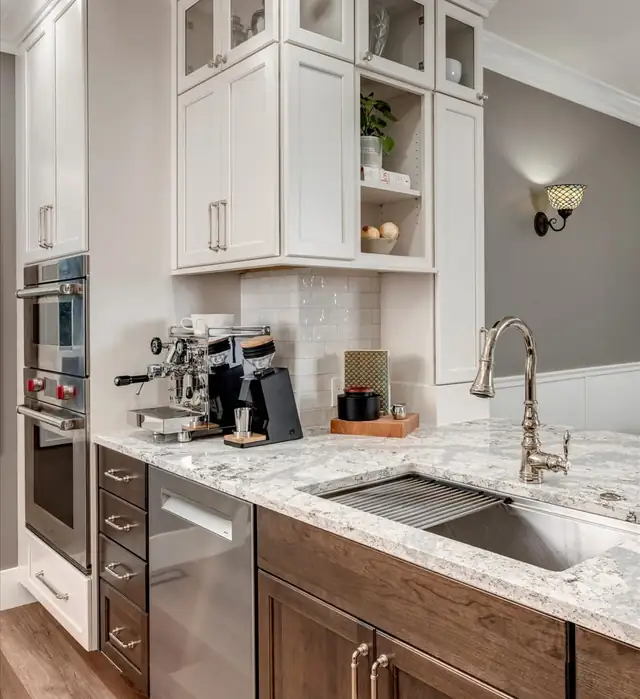 Kitchen coffee station with stacked wall ovens, granite counter, workstation sink and walnut-tone lower cabinets