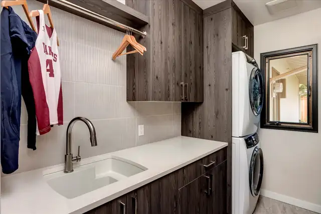 Laundry room remodel with dark wood-grain cabinets, hanging rod, utility sink and stacked washer and dryer