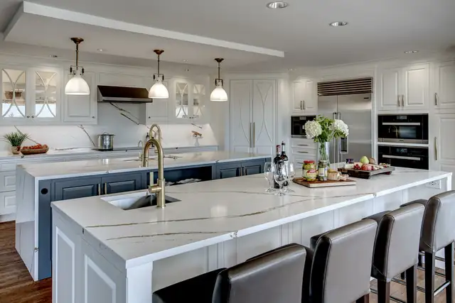 Double island kitchen with white cabinets, marble-look counters, glass pendants and built-in refrigeration