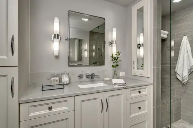 Sammamish primary bath with white cabinetry, a framed mirror, slim wall sconces and a gray tiled shower