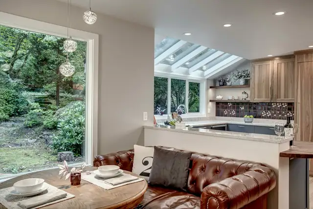 Eat-in kitchen nook with a leather banquette, skylights, wood cabinets and a large window onto the trees
